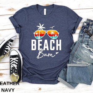 Pode incluir: Uma camiseta azul marinho heather com um gr&aacute;fico branco de &oacute;culos de sol com palmeiras e o texto "Beach Bum" com um cora&ccedil;&atilde;o.