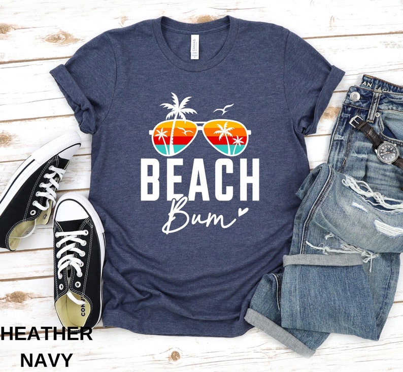 Pode incluir: Uma camiseta azul marinho heather com um gr&aacute;fico branco de &oacute;culos de sol com palmeiras e o texto "Beach Bum" com um cora&ccedil;&atilde;o.