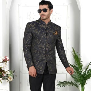May include: A dark navy suit with a floral pattern in gold. The suit includes a mandarin collar jacket with a pocket square and black dress pants. The person is wearing black loafers and sunglasses.