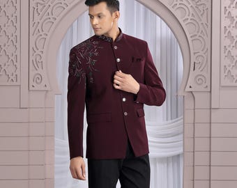 May include: A burgundy jacket with detailed shoulder embroidery, worn with black trousers. The jacket has a mandarin collar and button fastening. The outfit is completed with black dress shoes. The background features an ornate archway.