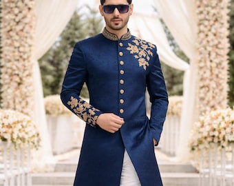 Puede incluir: Chaqueta larga azul marino con bordados dorados en el cuello, hombros y mangas. La chaqueta tiene botones dorados y se combina con pantalones blancos y zapatos color crema. El atuendo es adecuado para eventos formales.