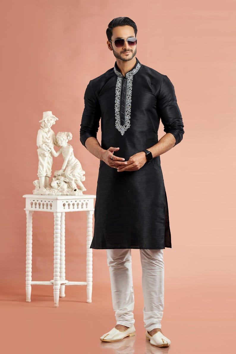 May include: Black kurta with white embroidery on the collar and a matching pair of white pants. The long-sleeved kurta is paired with white shoes. The outfit is worn by a person wearing sunglasses.