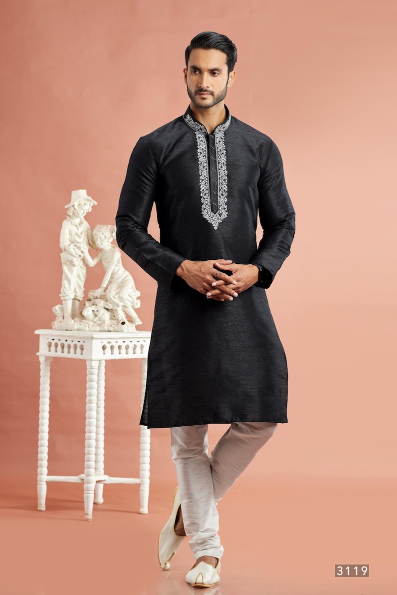 May include: A black kurta with white embroidery around the collar and neckline, paired with white pants. The long-sleeved tunic has a straight cut. The outfit is worn with white shoes. The image is set against a peach background.