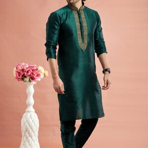 May include: A dark teal kurta pajama set. The long-sleeved kurta features gold embroidery around the collar and down the front. The matching pajama pants are a similar dark teal color. The person is wearing sunglasses and gold-colored shoes.