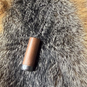 May include: A brown and silver bottle stopper with a chain and ring. The stopper has a cylindrical shape with a silver band at the base. The chain is attached to a silver ring.