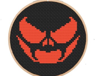 May include: A black and orange cross-stitch embroidery of a jack-o'-lantern face in a wooden embroidery hoop.