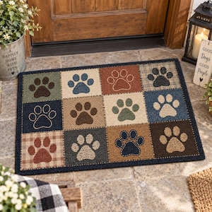 May include: A rectangular doormat featuring a grid of twelve squares, each displaying a unique paw print design. The squares alternate between various textured patterns and solid colors including blue, brown, green, and tan, all bordered by a dark frame.