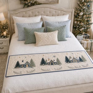 May include: A rectangular bed runner featuring a cream-colored fabric with a dark blue border. The runner displays three embroidered winter scenes of houses surrounded by snow-covered pine trees, stars, and snowflakes, with quilted detailing.