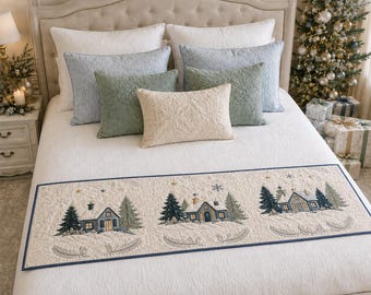 May include: A rectangular bed runner featuring a cream-coloured fabric with a dark blue border. The runner displays three embroidered winter scenes of houses surrounded by snow-covered pine trees, stars, and snowflakes, with quilted detailing.