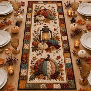 May include: A rectangular fabric table runner featuring a patchwork border and a central cream panel decorated with appliqued pumpkins, autumn leaves, berries, and a vintage-style lantern. The design includes various plaid and floral fabric patterns.