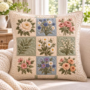 May include: A square throw pillow featuring a grid of nine embroidered floral panels. The design includes various flowers like daisies, roses, and greenery in shades of pink, blue, yellow, and green on a cream-colored quilted fabric background.
