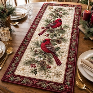 May include: A rectangular quilted table runner featuring a cream-colored center with two red cardinal birds perched on pine branches with pinecones and white berries. The runner has a deep red border decorated with green holly and red berries.