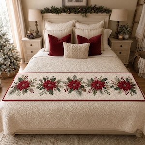 May include: A rectangular bed runner featuring a cream-colored quilted fabric base with a repeating pattern of red poinsettia flowers, green pine branches, and small brown pinecones, finished with a thin red border trim along the edges.