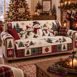 Peut inclure: Une housse de canapé couleur crème avec un motif matelassé orné de bonhommes de neige en appliqué portant des chapeaux et des écharpes, entourés de sapins, de flocons de neige et de houx brodés. La bordure présente des carrés en patchwork.