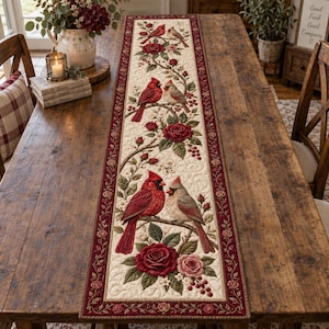Puede incluir: Un camino de mesa rectangular con un panel central de color crema que presenta un patrón repetitivo de cardenales rojos, pájaros grises y rosas de color rojo intenso sobre ramas con hojas. Tiene un borde ancho de color rojo oscuro con rosas.