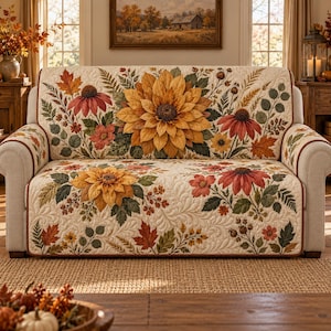 May include: A cream-colored quilted sofa cover featuring a vibrant botanical print of large yellow sunflowers, reddish-orange coneflowers, and various autumn-toned leaves and ferns. The fabric has a detailed stitched texture throughout the design.