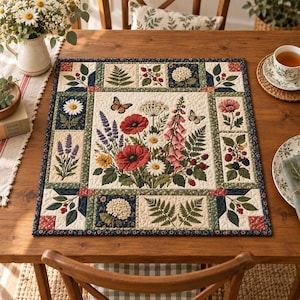 May include: A rectangular quilted fabric mat featuring a central botanical illustration of red poppies, white daisies, and pink foxgloves with two butterflies. The border consists of smaller square and rectangular panels displaying ferns, berries, and flowers.