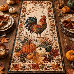 May include: A rectangular quilted table runner featuring a central rooster illustration surrounded by pumpkins, gourds, and autumn leaves in shades of orange, brown, and green. The border is decorated with a repeating pattern of fall foliage.