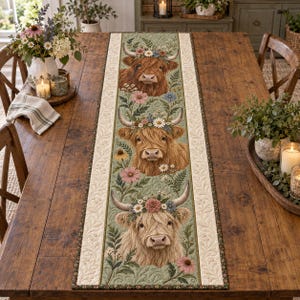 Peut inclure: Un chemin de table matelassé rectangulaire orné de trois portraits de vaches Highland alignés verticalement. Chaque vache porte une couronne de fleurs avec des marguerites sur un fond vert sauge. La bordure est crème à motifs de feuilles.