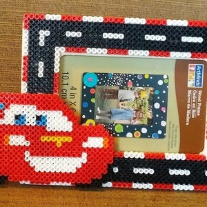 Può includere: Una cornice per foto fatta a mano con un design di auto da corsa rossa realizzata con perline colorate. La cornice ha un bordo nero, bianco e rosso e contiene una foto. La cornice misura 10,1 cm per 15,2 cm.