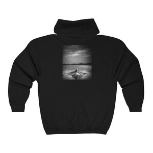 May include: Black and white photo of a person laying in a body of water. The person is wearing a swimsuit and has their arms outstretched. The photo is printed on a black hoodie.