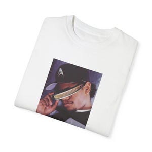 Puede incluir: Camiseta blanca con una imagen en blanco y negro de un hombre con una gorra de béisbol negra y gafas de sol futuristas.