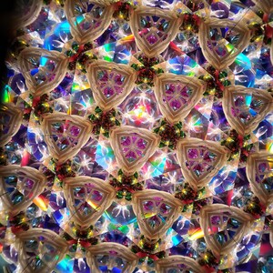 May include: A kaleidoscope image with a repeating pattern of white, pink, and green triangles. The background is a shimmering iridescent blue and purple.