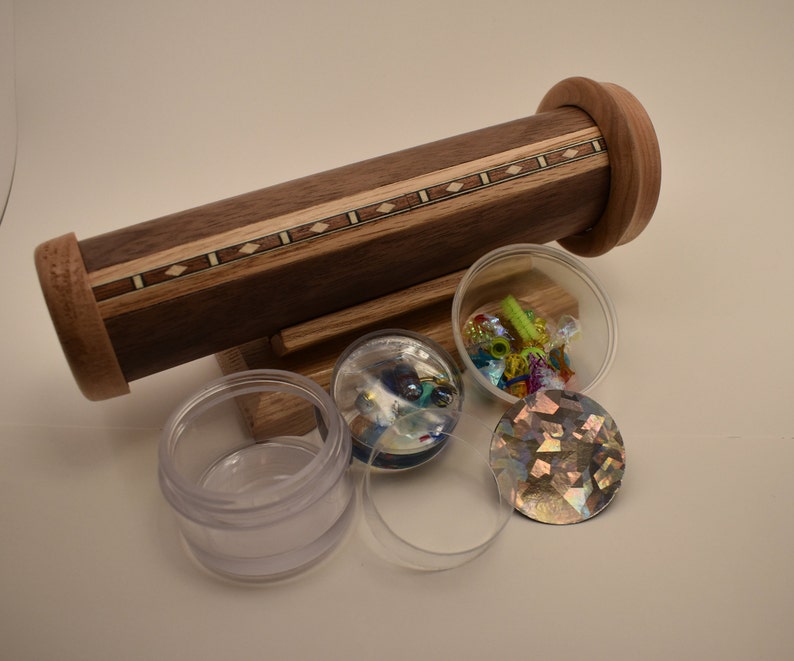 May include: A wooden kaleidoscope with a decorative inlay of wood and a stand. The kaleidoscope is surrounded by clear plastic containers filled with colorful glass beads and a iridescent glass disc.