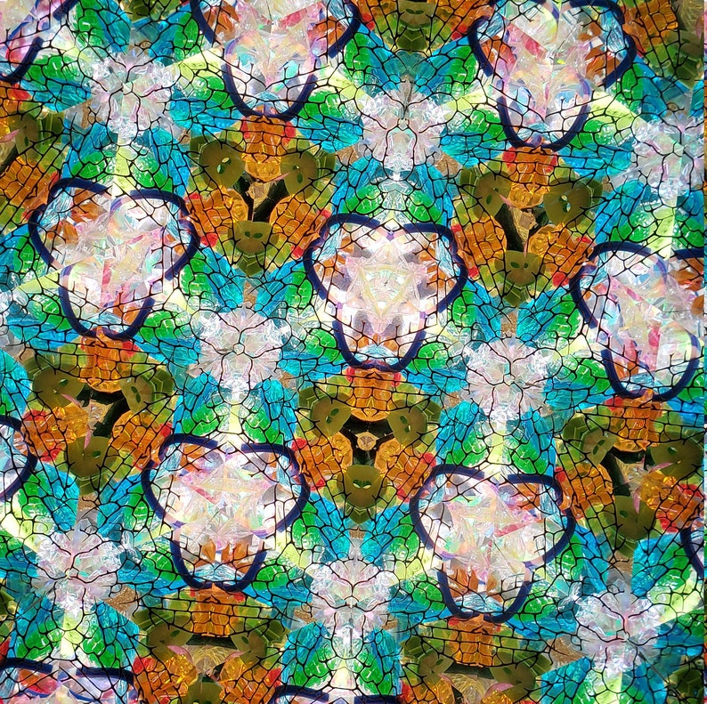 May include: Abstract kaleidoscope pattern with a repeating design of blue, green, orange, and white geometric shapes. The shapes are outlined in black and create a symmetrical pattern.
