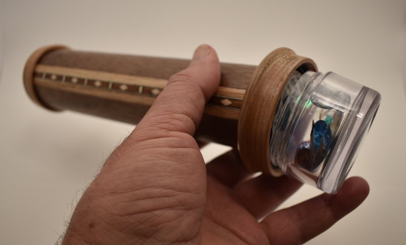 May include: A wooden kaleidoscope with a clear plastic viewing end. The kaleidoscope is decorated with a wood inlay pattern.