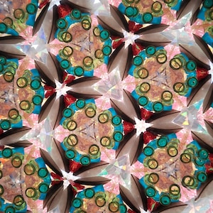 May include: A kaleidoscope image with a repeating pattern of teal, yellow, and red circles. The background is a shimmering, iridescent surface.