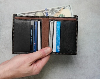 May include: A bi-fold wallet in black and brown leather, filled with credit cards and a hundred-dollar bill. The wallet is held open, showcasing the interior card slots and cash compartment. The wallet has a textured appearance.