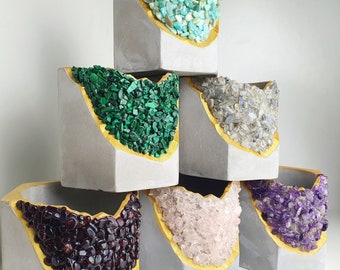 May include: A stack of six gray concrete planters, each with a unique gemstone filling and a gold-painted rim. Gemstones include turquoise, malachite, labradorite, garnet, rose quartz, and amethyst. The planters have a modern, geometric design.
