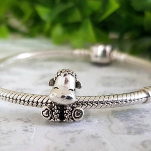 Puede incluir: Un brazalete de plata con un dije de plata de una oveja con corazones en sus patas.