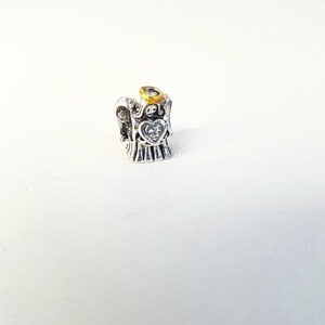 May include: Silver angel charm with a gold halo and a clear crystal heart. The charm is designed to be used on a bracelet or necklace.
