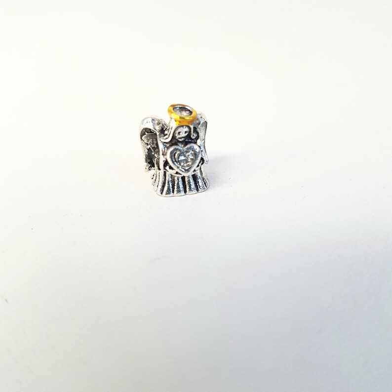 May include: Silver angel charm with a gold halo and a clear crystal heart. The charm is designed to be used on a bracelet or necklace.