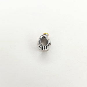 May include: Silver charm in the shape of an angel with a yellow halo. The angel is holding its hands together in prayer.
