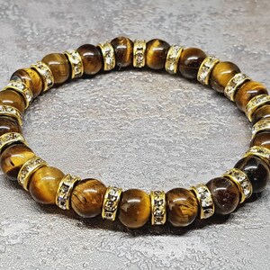 May include: A brown tiger's eye gemstone bracelet with gold accents and clear crystal beads.