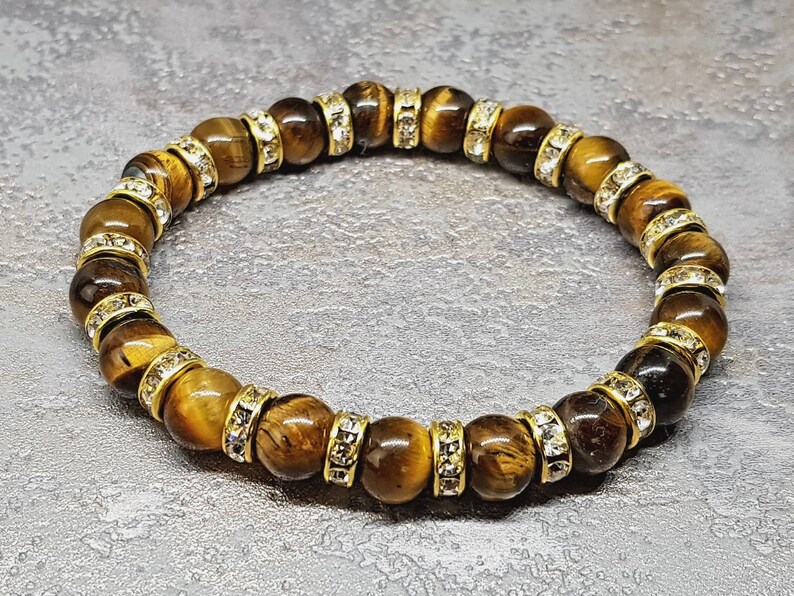 May include: A brown tiger's eye gemstone bracelet with gold accents and clear crystal beads.