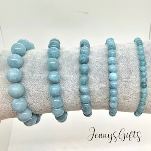 May include: Five aquamarine beaded bracelets of varying lengths, displayed on a hand. The bracelets are made of smooth, round beads with a light blue color.