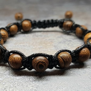 Può includere: Un braccialetto in corda nera con perline di legno marrone. Il braccialetto è annodato e ha un design semplice.