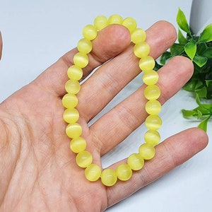 May include: A yellow beaded bracelet with a cat's eye finish. The bracelet is made of round beads and is strung on elastic.