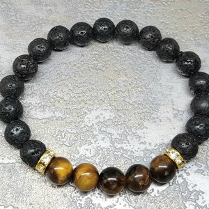 Puede incluir: Un brazalete de cuentas de lava negra y ojo de tigre con separadores dorados. El brazalete tiene un cord&oacute;n el&aacute;stico extensible.