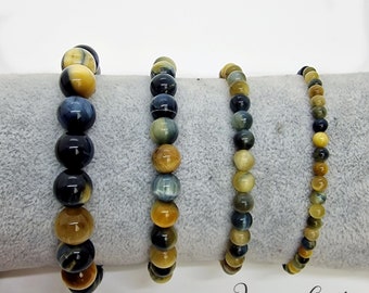 Puede incluir: Cuatro pulseras de cuentas con piedras de ojo de tigre de diferentes tamaños. Las cuentas muestran una mezcla de tonos amarillo dorado, marrón y azul oscuro. Las pulseras se exhiben sobre una superficie gris, con el texto "JennyS Gifts" en la esquina inferior derecha.