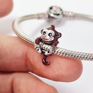 Peut inclure: Un charm argenté représentant un singe marron et argenté. Le singe souriant est accroché à un bracelet en argent. Le charm est détaillé avec des accents marron et argenté. Bijou de bracelet.