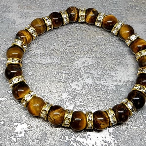 May include: A brown tiger's eye gemstone bracelet with gold accents and clear crystal beads.