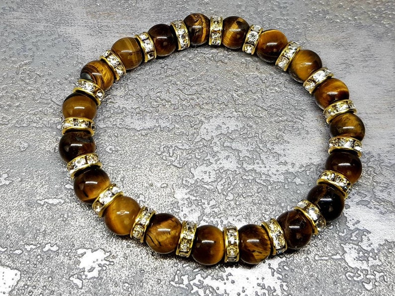 May include: A brown tiger's eye gemstone bracelet with gold accents and clear crystal beads.