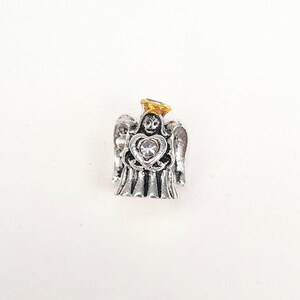 May include: Silver angel charm with a gold halo and a clear crystal heart. The angel is holding the heart in its hands.