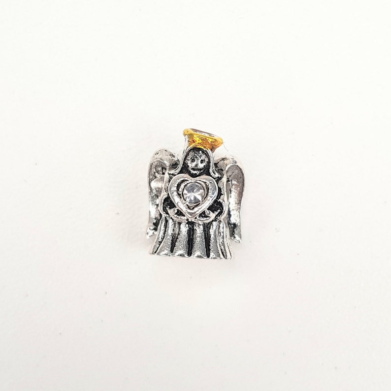 May include: Silver angel charm with a gold halo and a clear crystal heart. The angel is holding the heart in its hands.