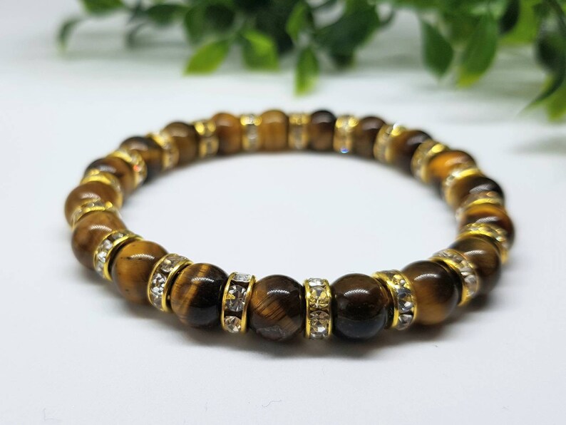 May include: A brown tiger's eye gemstone bracelet with gold accents and clear rhinestones.